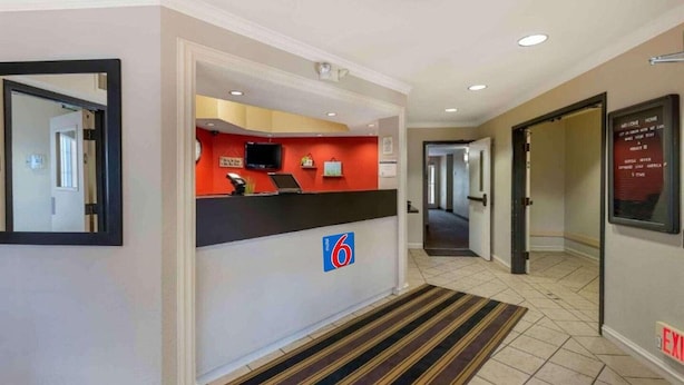Zona de recepción de un hotel, con un mostrador de recepción, un letrero que indica la habitación número 6 y un cartel de bienvenida en la pared.