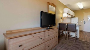 Una habitación de hotel con un aparador de madera, televisor, escritorio y dos sillas, y un espejo.