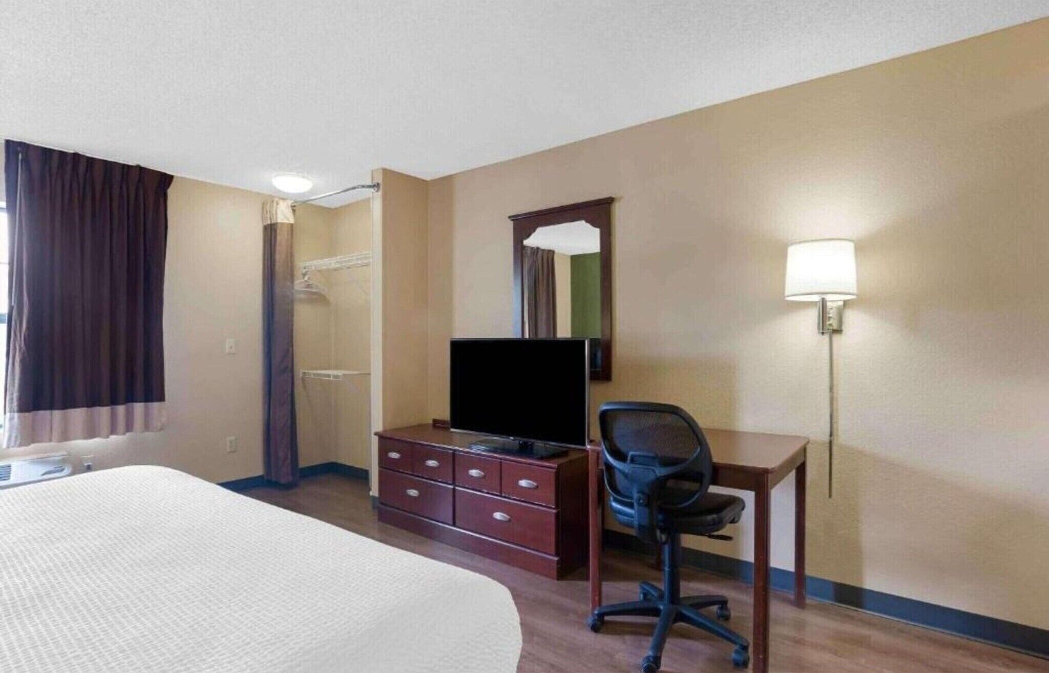 Ein Hotelzimmer mit Bett, Schreibtisch mit Stuhl, Fernseher, Lampe und Spiegel.