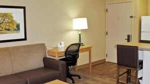 Una habitación de hotel con un sofá de cuero marrón, un escritorio de madera con una lámpara, una computadora y una silla.