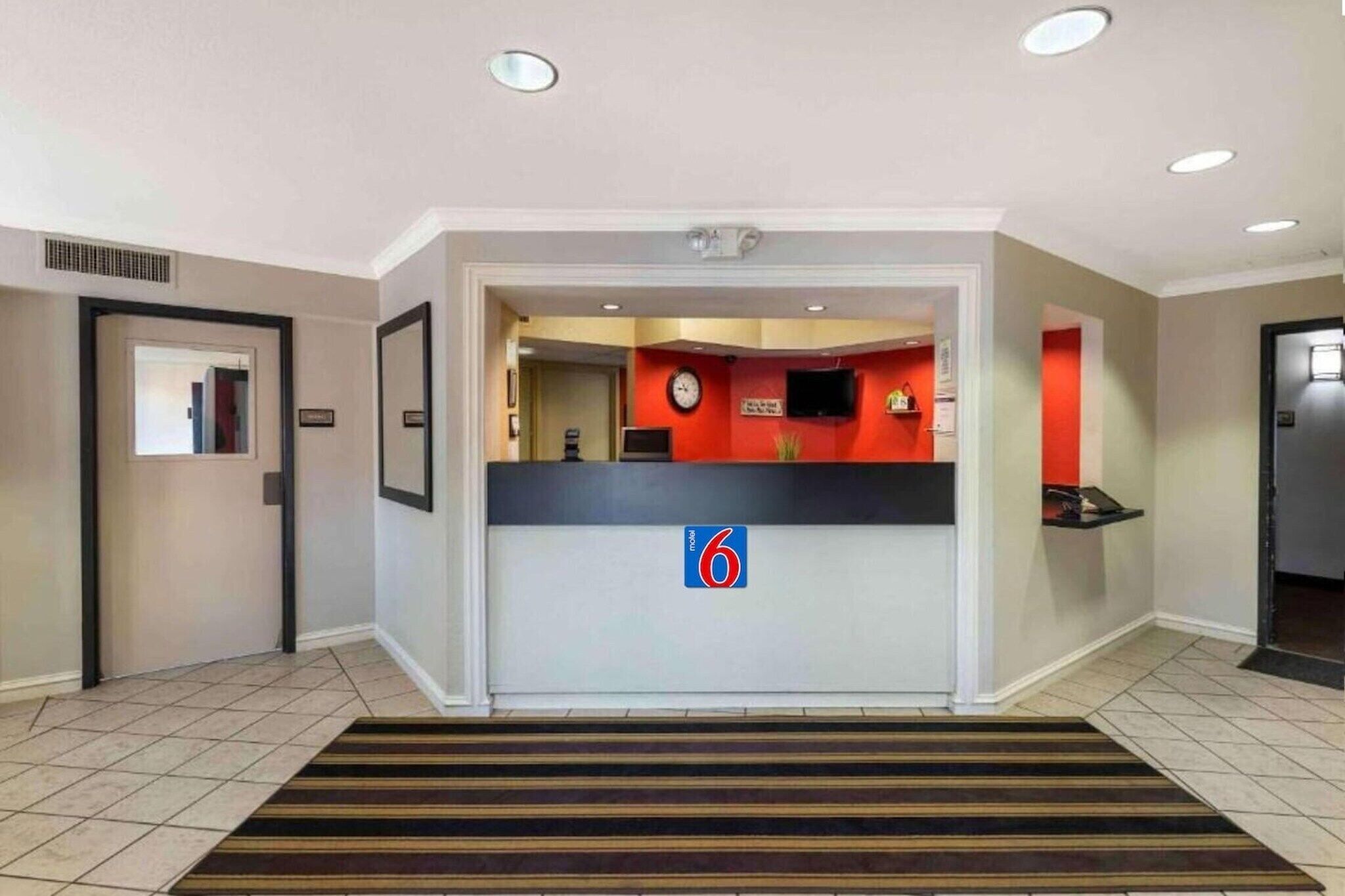 Uma área de recepção de hotel com um balcão, um relógio e uma placa indicando o quarto número 6.