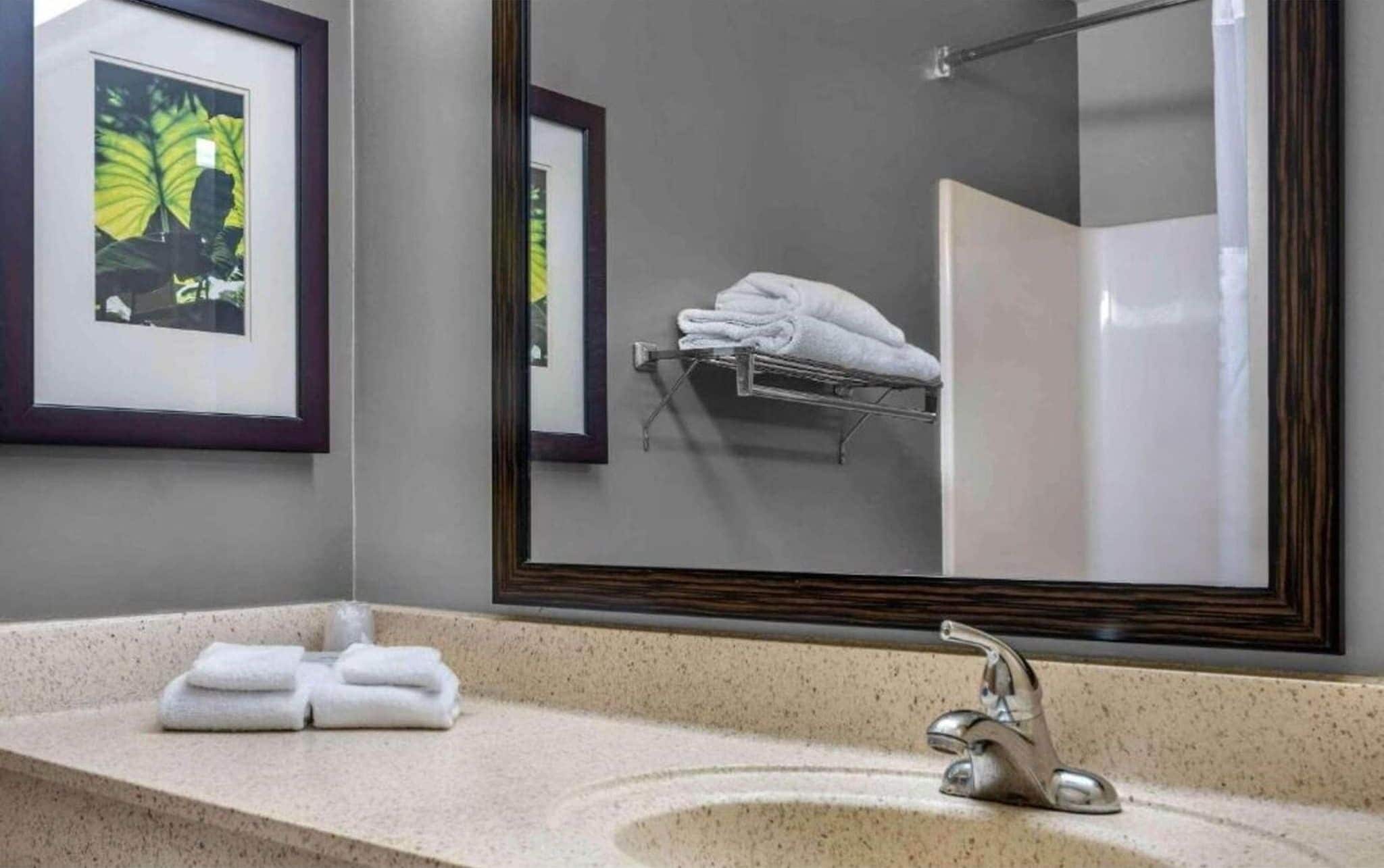 Un baño con lavamanos, espejo y toallero.