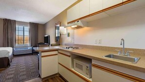 Una habitación de hotel compacta con kitchenette, una cama, televisión y ventana con cortinas.