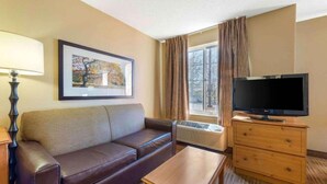 Habitación de hotel con sofá, televisor, una mesita, lámpara y un cuadro en la pared.