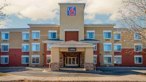Un motel con un llamativo letrero con el número '6', una entrada al vestíbulo y un estacionamiento.