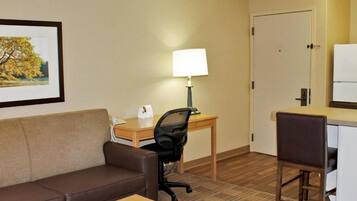 Quarto de hotel com sofá de couro marrom, escrivaninha de madeira com luminária, computador e pequena mesa de madeira.