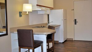 Una kitchenette pequeña con una encimera, un lavabo, un refrigerador y una silla.
