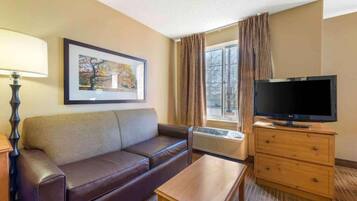 Habitación de hotel con sofá, televisor, una mesita, lámpara y un cuadro en la pared.
