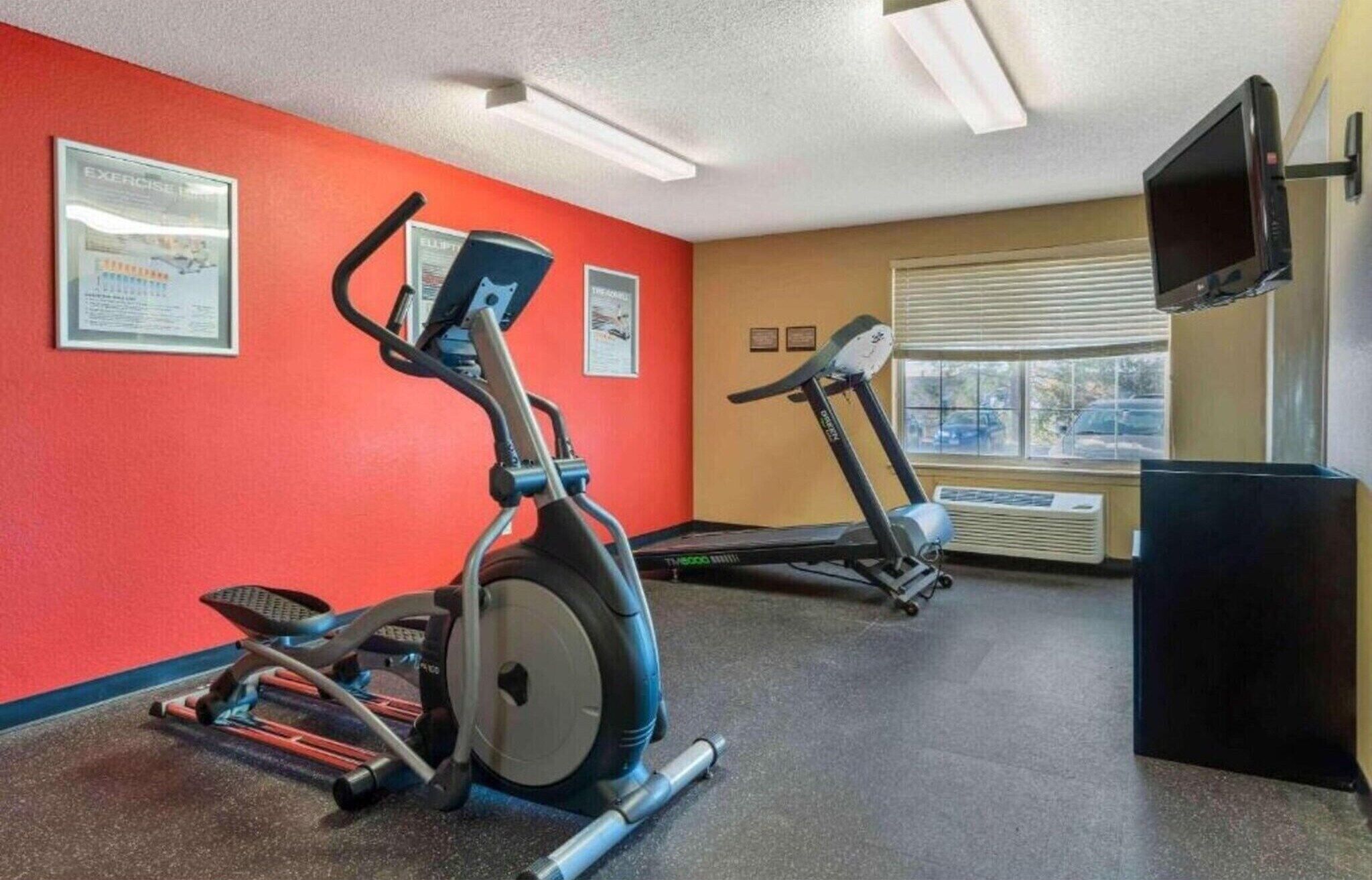 Uma academia com esteiras, uma máquina elíptica e um banco de musculação.