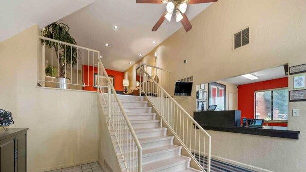 Un vestíbulo de hotel con escalera, mostrador de recepción y ventilador de techo.
