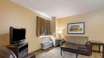 A hotel room with a flat-screen TV, a sofa, a coffee table, a lamp, a heater, and a framed picture on the wall.