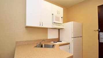 Una cucina compatta con mobili bianchi, un forno a microonde, un frigorifero e un lavello.