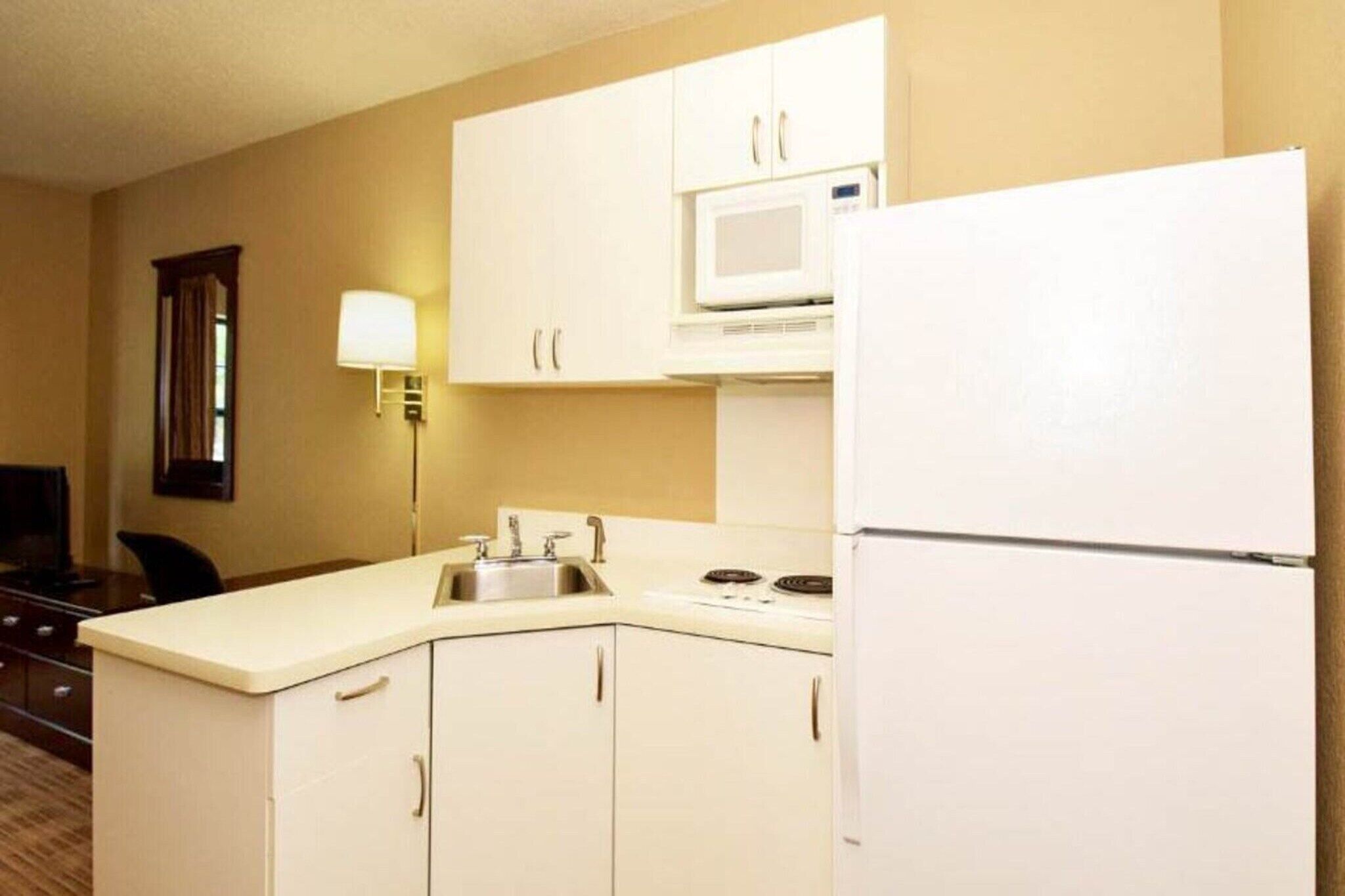 A compact kitchen with a microwave, refrigerator, sink, and cabinets.