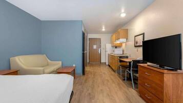 A hotel room with a bed, a desk, a chair, a television, and a kitchenette.