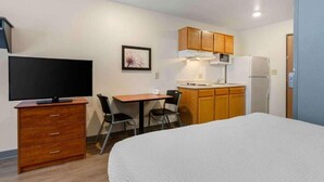Ein kleines Hotelzimmer mit Bett, Fernseher, Schreibtisch mit Stühlen, einer Küchenzeile und Holzausbau.