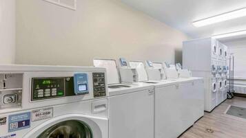 A laundry facility with multiple washing machines and dryers, a digital display, and a QR code for laundry services.