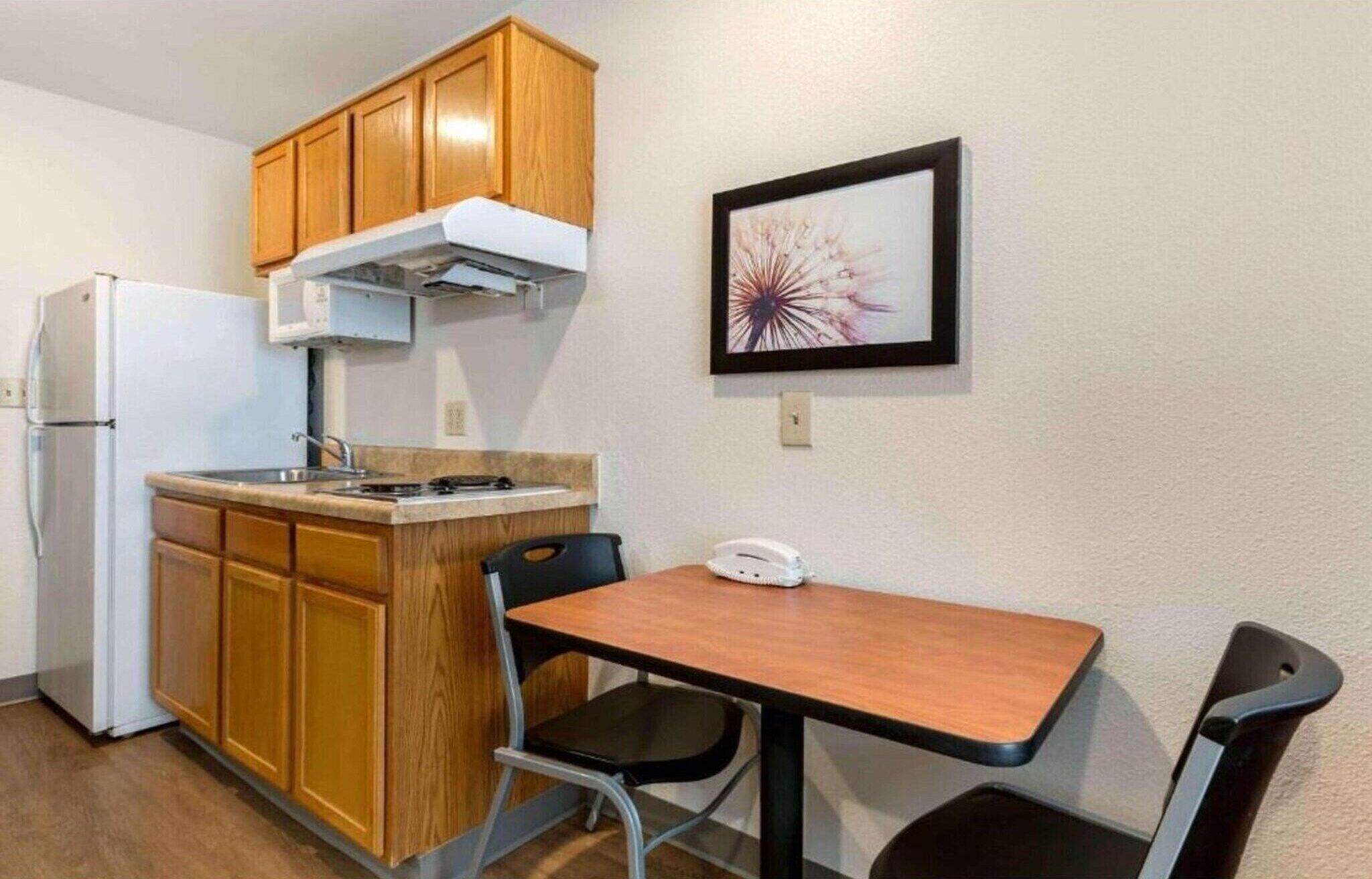 A compact kitchen with wooden cabinets, a white refrigerator, a stove, and a small dining table with two chairs.