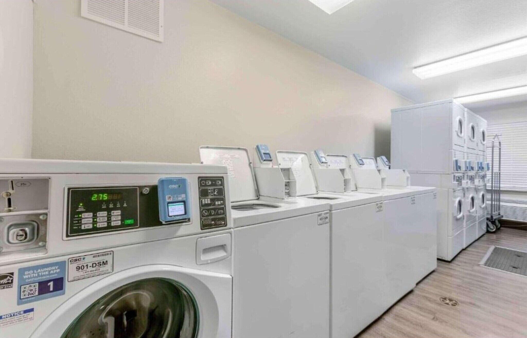 Un cuarto de lavandería con varias lavadoras y secadoras, una pantalla digital y un código QR para servicios de lavandería.