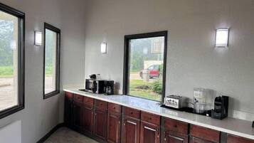 A kitchen with a microwave, toaster, and coffee maker on the counter, wooden cabinets, and a window with a view of a red car outside.