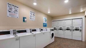 Un lavadero con varias lavadoras y secadoras, piso de baldosas y carteles informativos en las paredes.