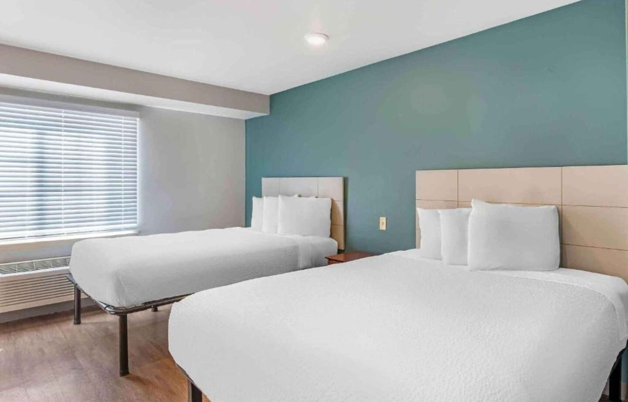 Een hotelkamer met twee bedden, een raam met zonwering, een wandverwarming en een plafondlamp.