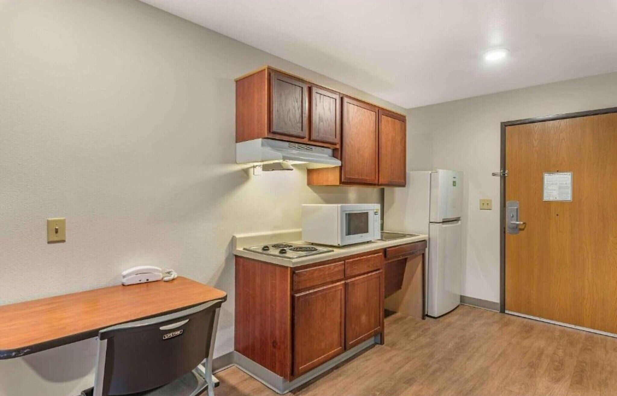 A compact kitchenette with wooden cabinets, a microwave, a refrigerator, and a small table.