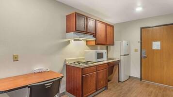A compact kitchenette with wooden cabinets, a microwave, a refrigerator, and a small table.