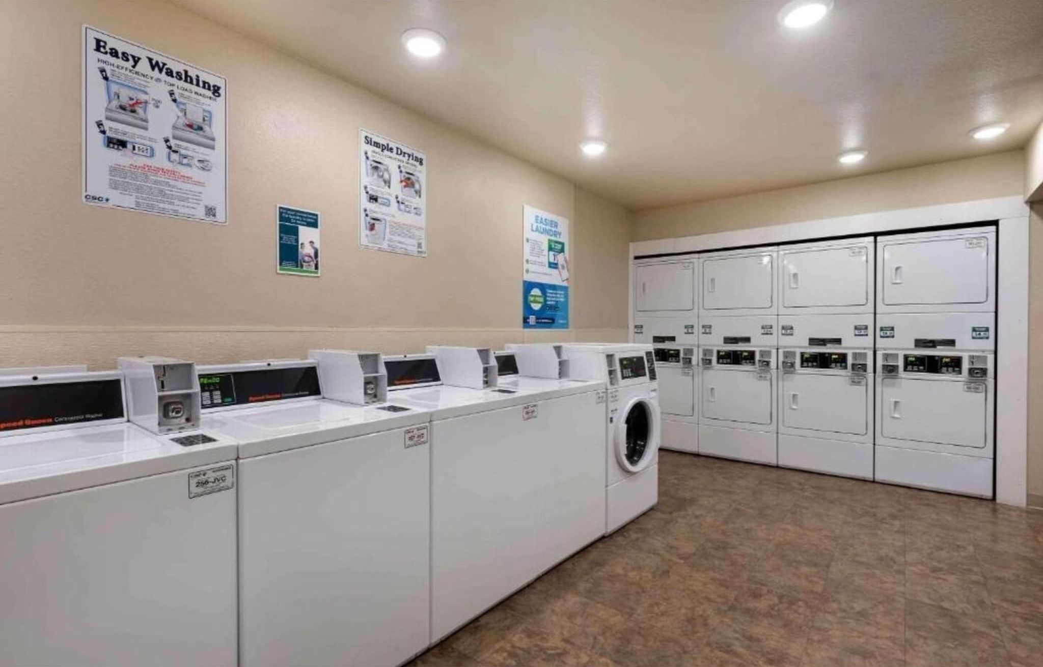 A laundry facility with multiple washing machines and dryers, a tiled floor, and informational posters on the walls.