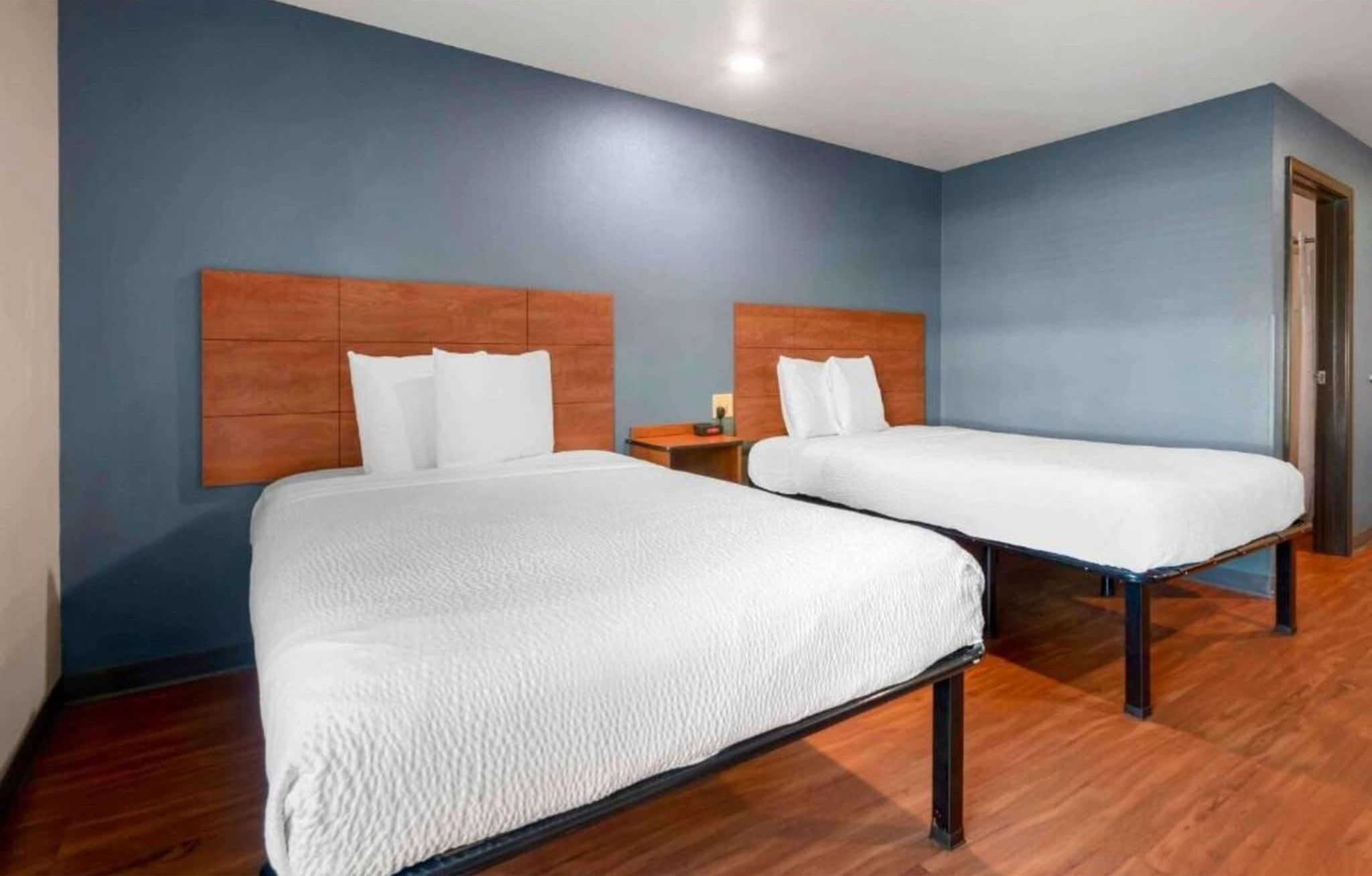 A hotel room with two beds, wooden headboards, and a blue wall.