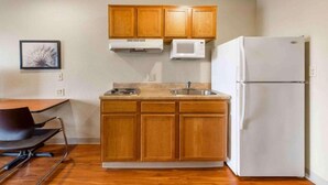 Une cuisine de taille réduite, avec des meubles en bois, un réfrigérateur blanc, un four à micro-ondes, un évier et une chaise.