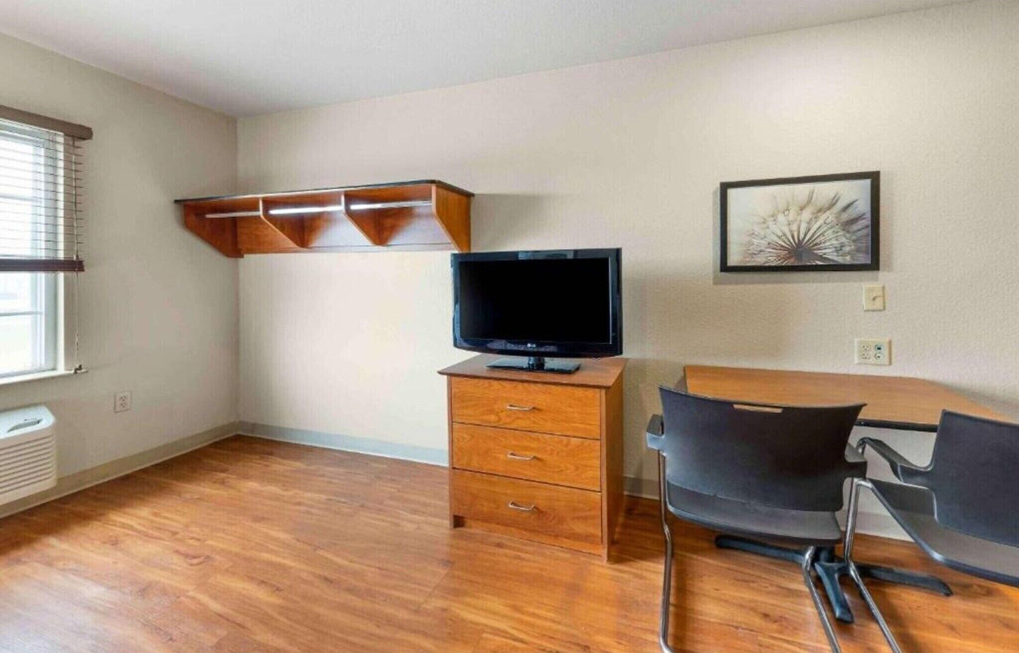A room with a wooden floor, a TV on a wooden cabinet, a chair, and a picture on the wall.