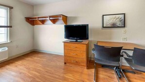 Une pièce avec un plancher en bois, un téléviseur posé sur un meuble en bois, une chaise et un tableau accroché au mur.