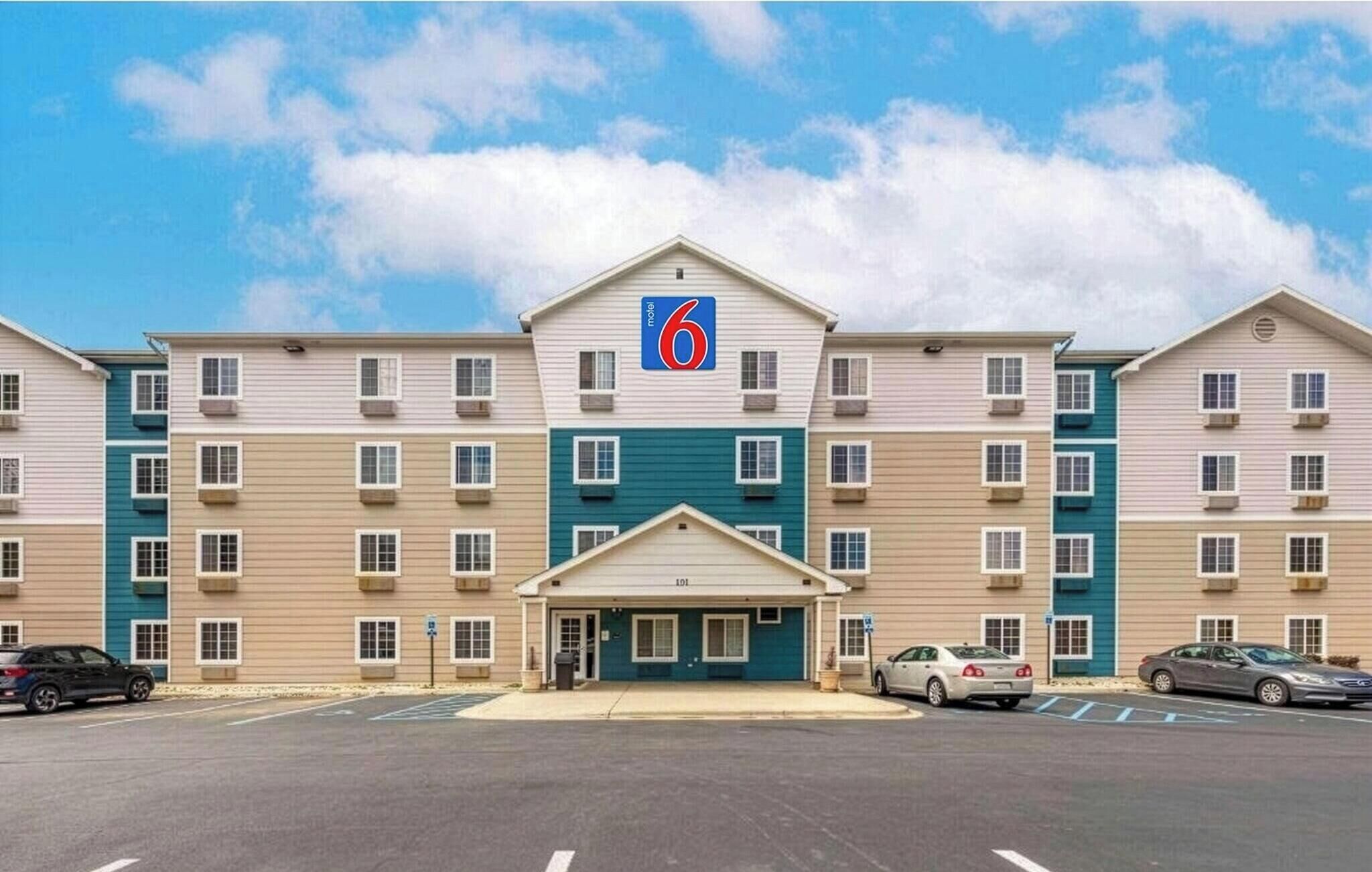 Un motel con entrada central, varios pisos y estacionamiento.