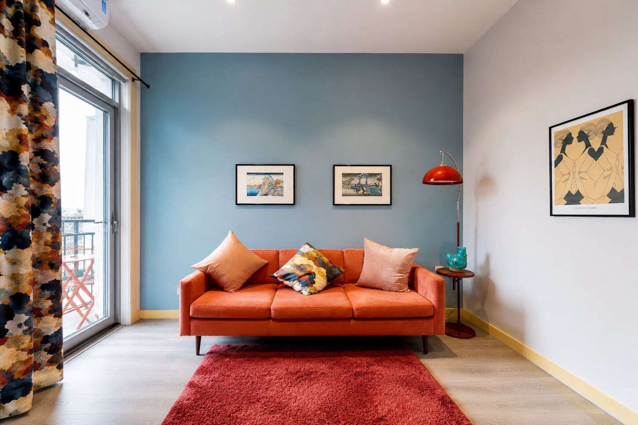 A room with a blue wall, a red sofa, a red rug, and two framed pictures.