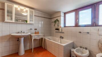 Ein Badezimmer mit Standwaschbecken, Badewanne, Bidet und einem Fenster.