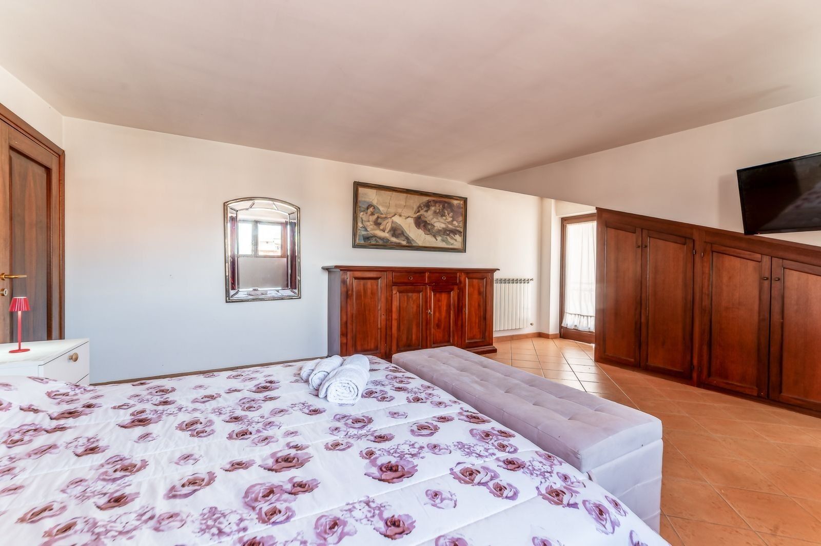 A bedroom with a bed, a wooden wardrobe, a painting, and a television.
