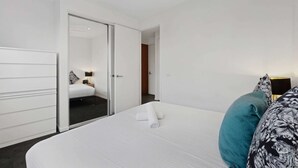 Ein Hotelzimmer mit Bett, Kleiderschrank und einem durchgehenden Türrahmen sichtbarem Badezimmer.