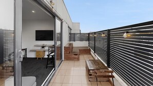 Ein moderner Balkon mit Glastür zu einem Innenraum, einer Holzbank und einem Metallgeländer.