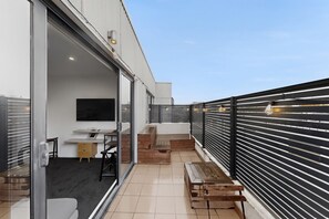 A modern balcony with a glass door leading to an interior space, a wooden bench, and a metal railing. - City-View 1-Bed Apartment Near Central Park (Richmond)