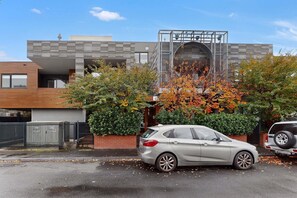 Ein modernes, zweistöckiges Gebäude mit Garage, einem davor parkenden Auto und einem Baum mit Herbstlaub.