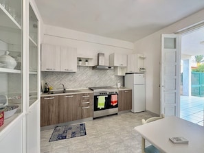 A modern kitchen with a built-in oven, a refrigerator, and a dining area with a table. - Villa in Santa Maria Del Focallo with 3 bedrooms sleeps 6 (Santa Maria Del Focallo)