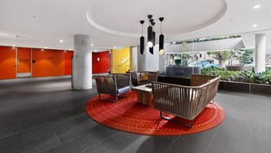 Eine moderne Lobby mit einer zentralen Sitzgelegenheit, einer großen Säule und Blick ins Freie.