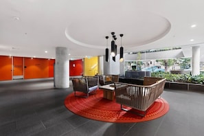 A modern lobby with a central seating area, a large pillar, and a view of the outdoors. - Exclusive 1-room apartment in an elevated location, just steps away from shops. (Southbank)