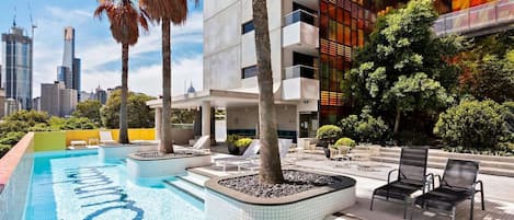 A rooftop swimming pool with lounge chairs and a cityscape view.