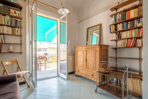 A room with a large open door leading to a balcony, a wooden cabinet, and a bookshelf filled with books. - La Terrazza in Centro, Genova (Genoa)