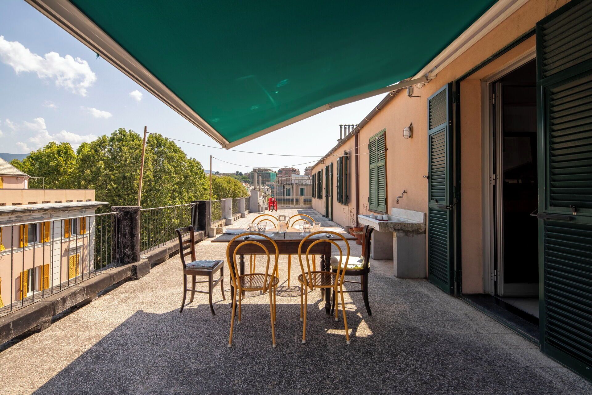 A terrace with a table and chairs, a green awning, and a view of the cityscape.