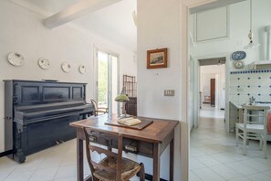 A dining area with a wooden table, chairs, a piano, and a kitchen in the background. - La Terrazza in Centro, Genova (Genoa)