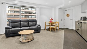 Ett modernt vardagsrum med en svart lädersoffa, ett runt soffbord i trä och en matplats med trästolar och ett litet bord.