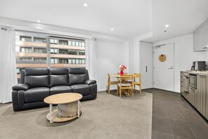 Ein modernes Wohnzimmer mit einem schwarzen Ledersofa, einem runden Couchtisch und einem Essbereich mit Holzsesseln und einem kleinen Tisch.
