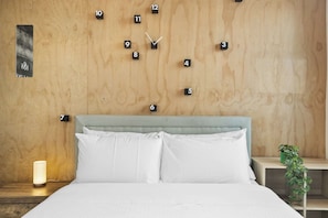 A bedroom with a wooden wall clock, a bed with white bedding, and a nightstand with a lamp. - Stylish 2-Bed Apartment by 888 Collins (South Melbourne)